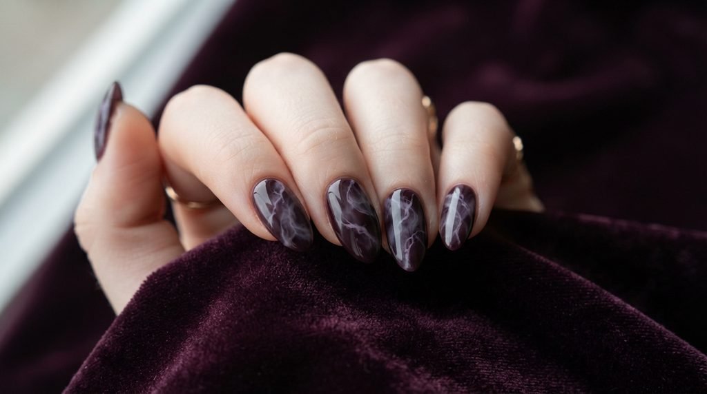 Deep plum smoky marble nails on an 18-year-old female hand against dark velvet background.