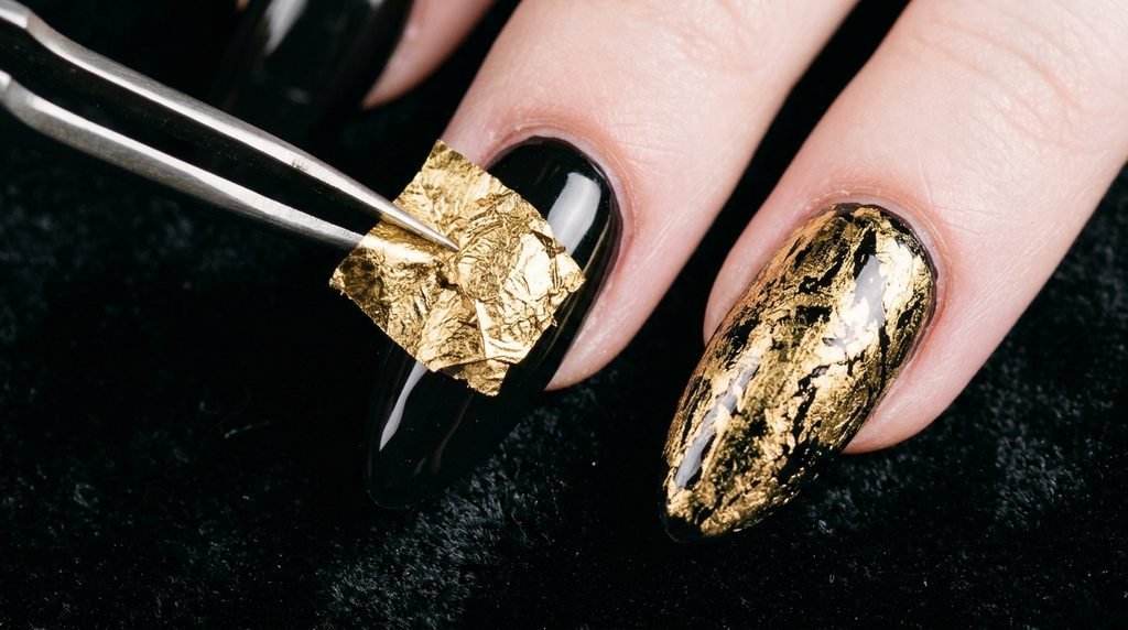 A close-up shot showing gold foil being applied to a glossy black almond nail, next to a finished foil-textured nail.