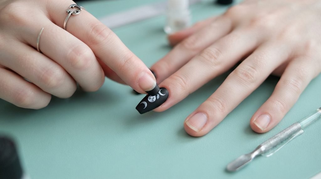 Female hand applying a dark celestial press-on nail with moon art to a natural nail.