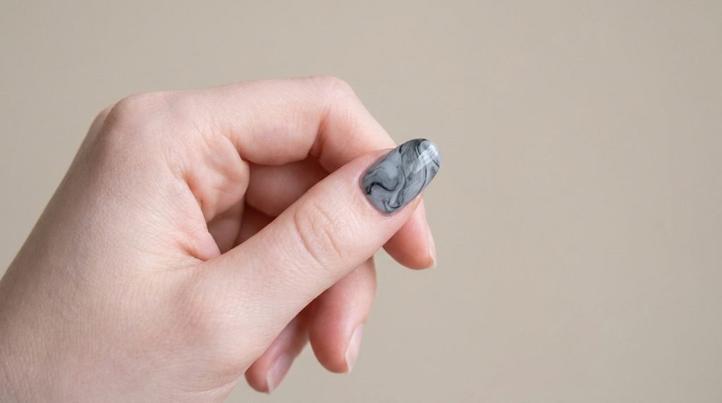 Applying a smoky black marble press-on nail to natural nail bed on an 18-year-old female hand.