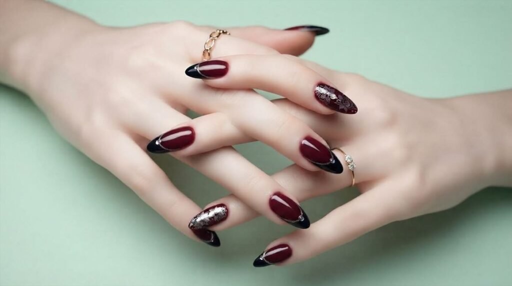 Close-up of an 18-year-old female hand with very white skin showing burgundy and black stiletto nails with silver floral designs.