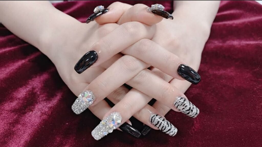 Close-up of an 18-year-old female hand with white skin showing glossy black almond nails with gold glitter ombré tips.