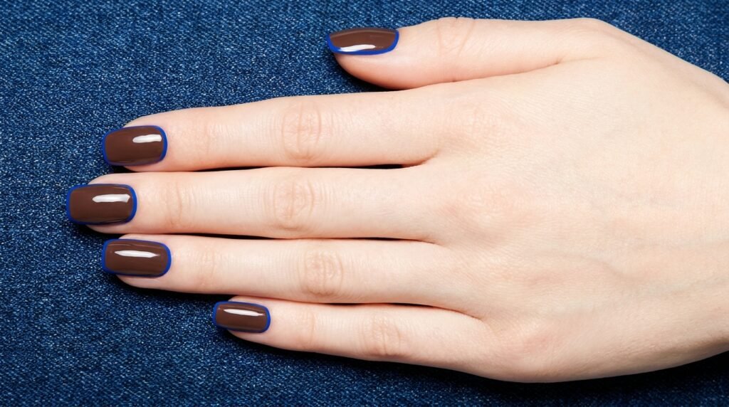 Medium square mocha brown nails with precise cobalt blue outline art on an 18-year-old female hand with white skin.