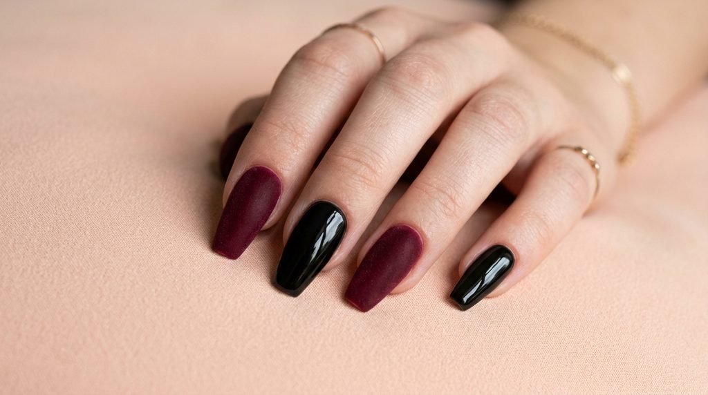 Matte burgundy and glossy black coffin nails on an 18-year-old white female hand on a peach background.