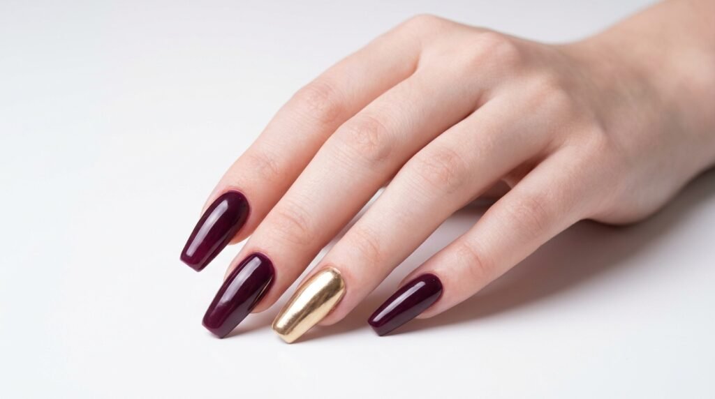 High-gloss burgundy acrylic coffin nails with one full gold chrome accent nail on a fair hand.