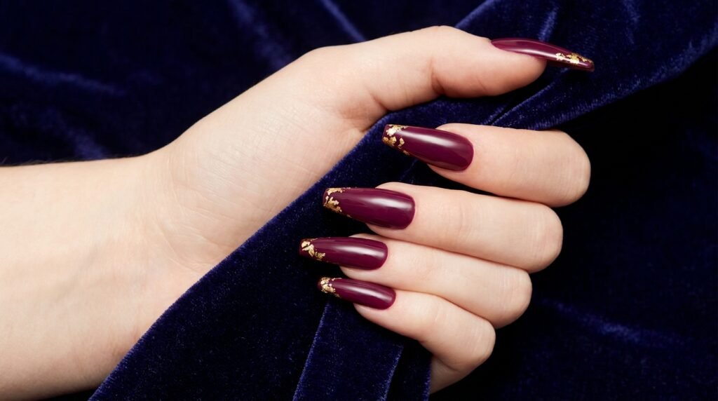 Tapered extra-long burgundy coffin nails framed with gold leaf flecks along the side edges.