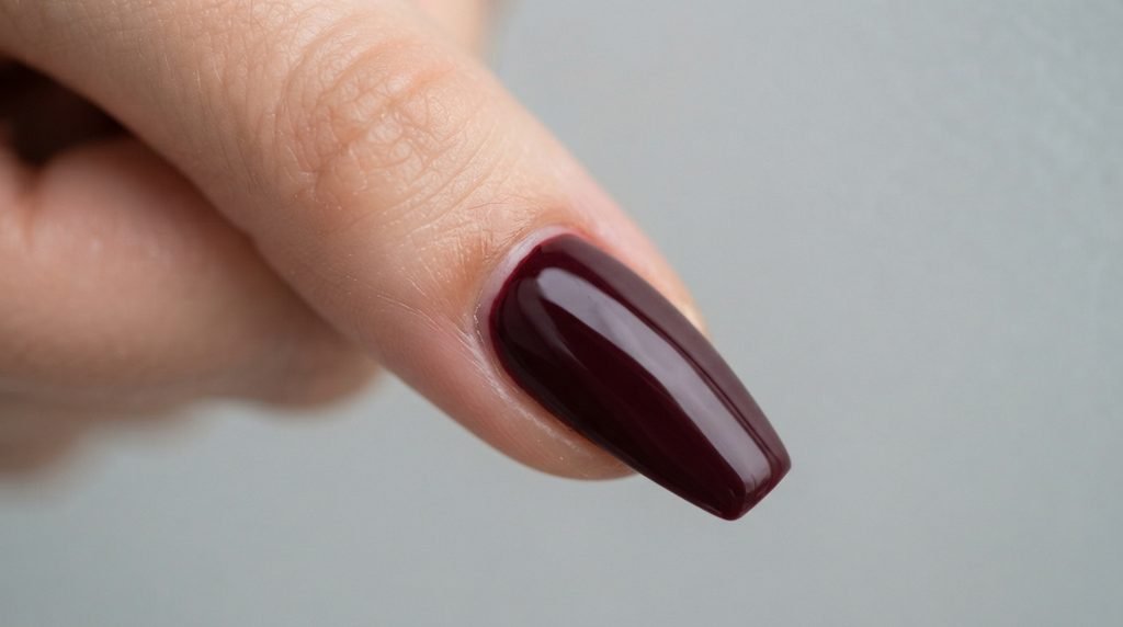 Macro shot of the flawless cuticle line of a deep burgundy coffin nail on an 18-year-old white hand.