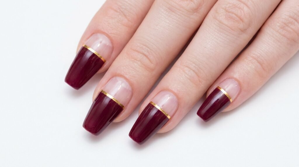 Negative space coffin nails with clear bases and burgundy top halves separated by a gold line.