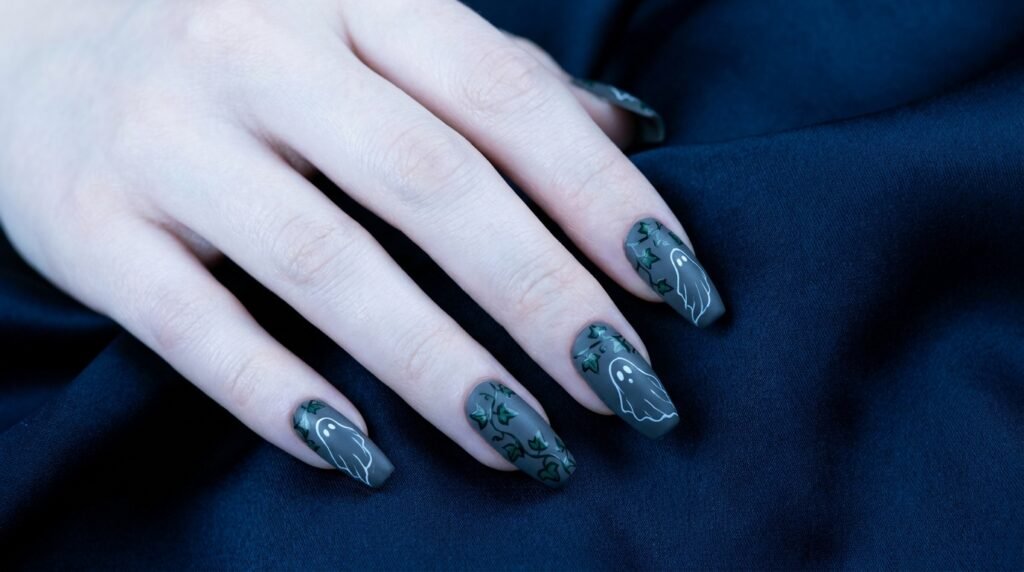 Coffin-shaped charcoal grey nails with white specters and green ivy line art on white skin.