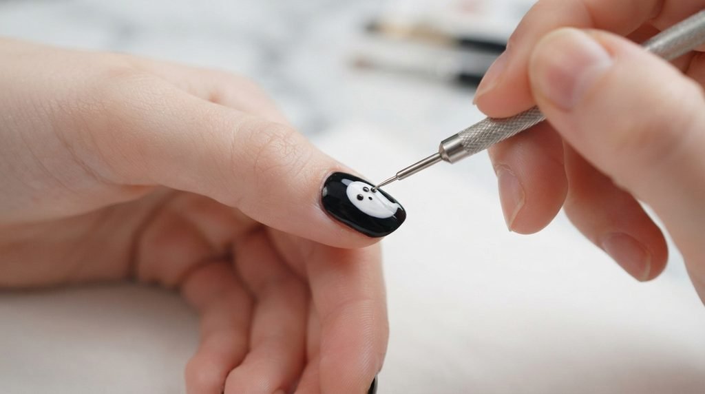 Dotting tool adding black dots to a painted white ghost on a nail with very white skin.