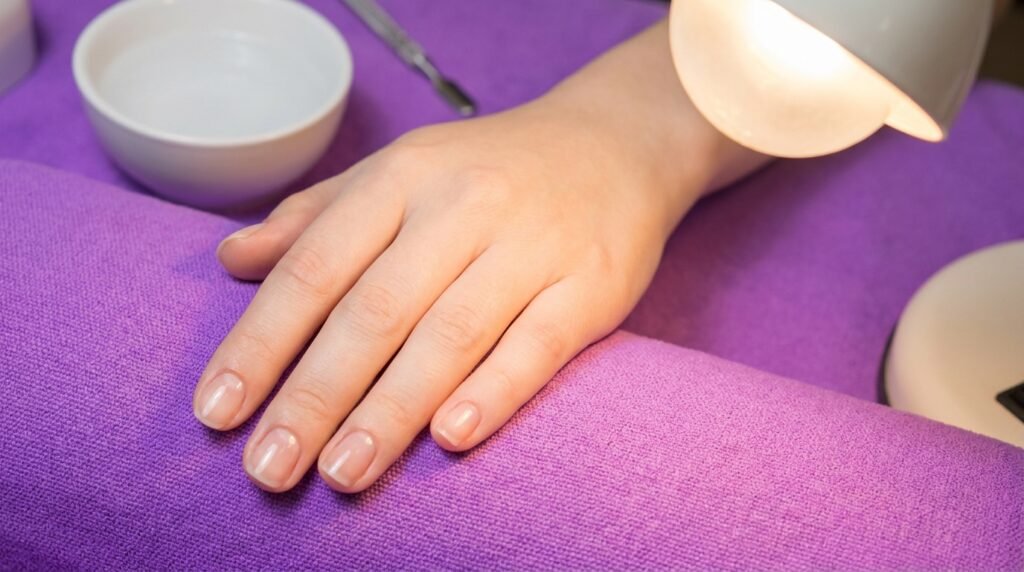 Clean natural nails on an 18-year-old white hand covered in a shiny clear base coat layer.