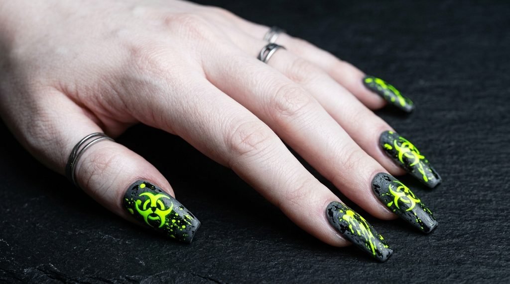 Coffin nails with dark gray base and glowing yellow-green biohazard symbols on slate background.