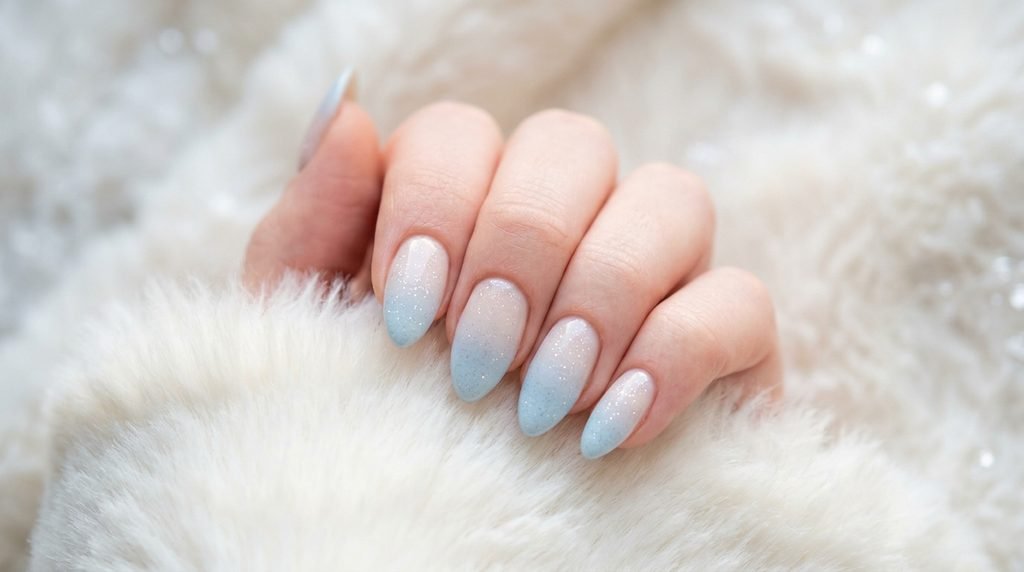 Close-up of almond blue ombré glitter nails on a female hand against a white faux fur background.