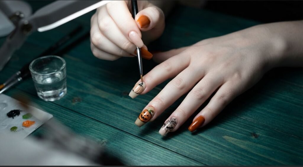 A female hand with white skin using a detail brush to paint pumpkin nail art on long coffin nails.