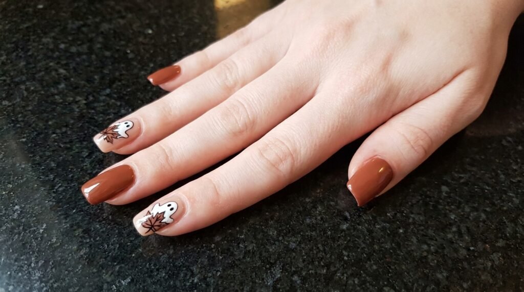 Squoval terracotta and nude nails with cute white ghosts and fall leaves on white skin.