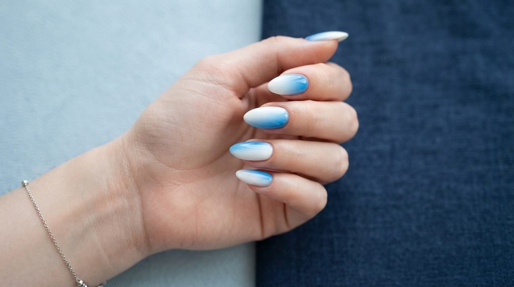 Close-up of a female hand showcasing nails with both reverse and vertical blue-to-white ombré gradients.