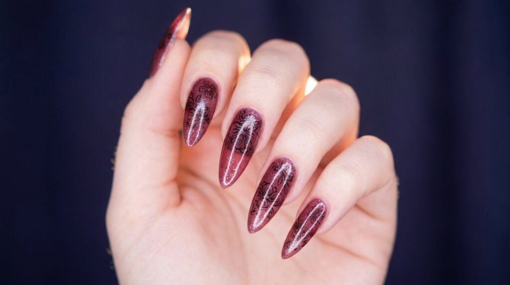 Jelly burgundy stiletto nails with black floral stamp art on an 18-year-old hand with very white skin.