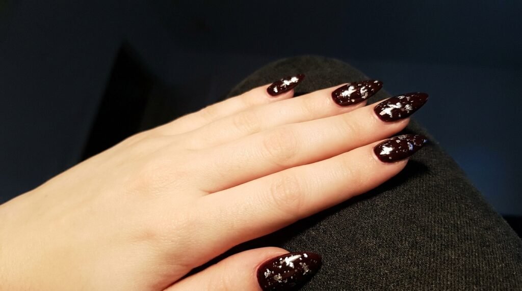 Silver foil accents over dark burgundy stiletto nails on an 18-year-old female hand with very white skin