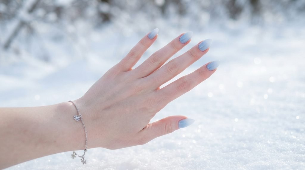Close-up of female hand with smooth blue to white ombré nails against blurry white snow background.