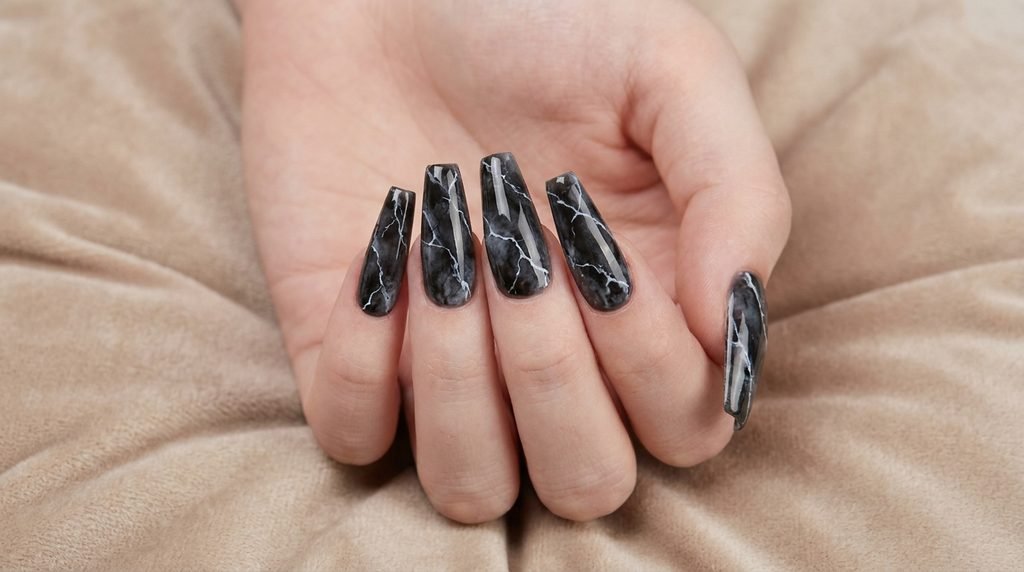 Long coffin smoky black marble nails displayed by an 18-year-old female hand on a beige background.