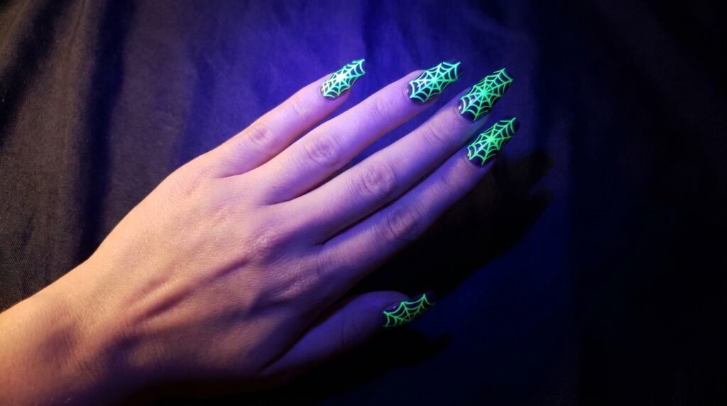 Neon green glowing spiderweb nail art under blacklight on an eighteen year old female hand.