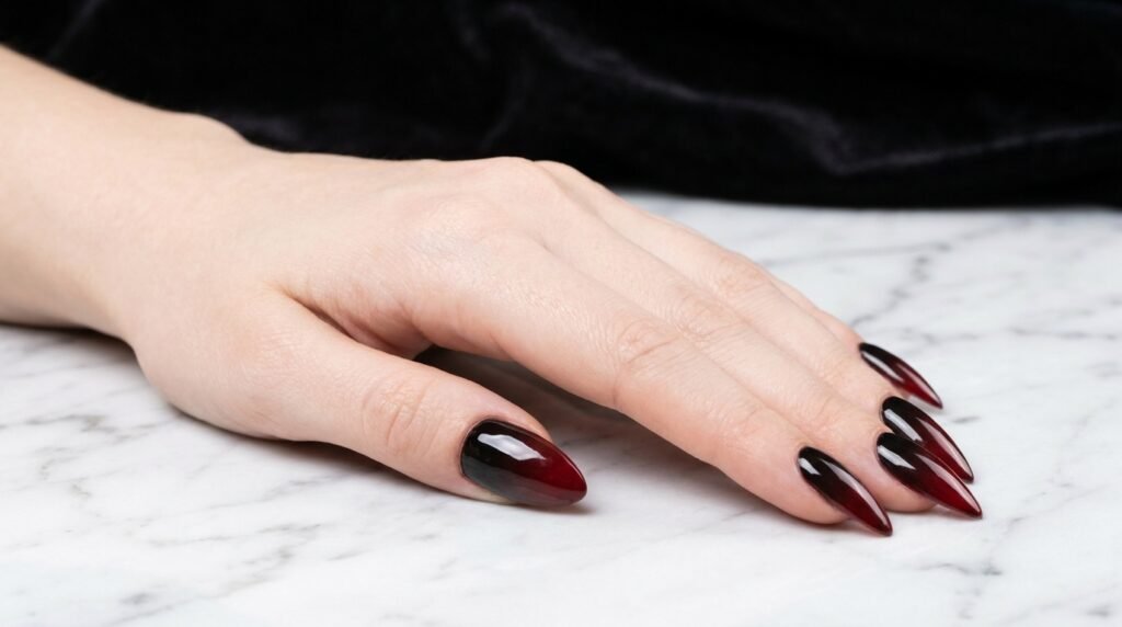 Smooth burgundy to black gradient on long stiletto nails on an 18-year-old female hand with very white skin.