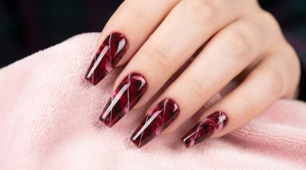 Long coffin nails featuring a red and black marble design with soft pink accents on a fair-skinned hand.