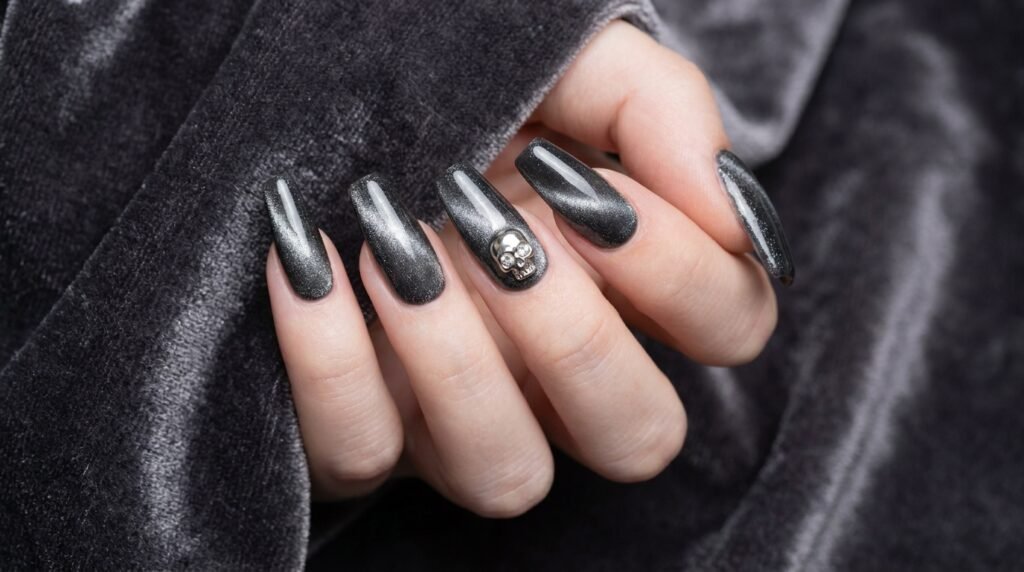 Charcoal magnetic velvet cat eye nails with silver skull charm on female hand with white skin.