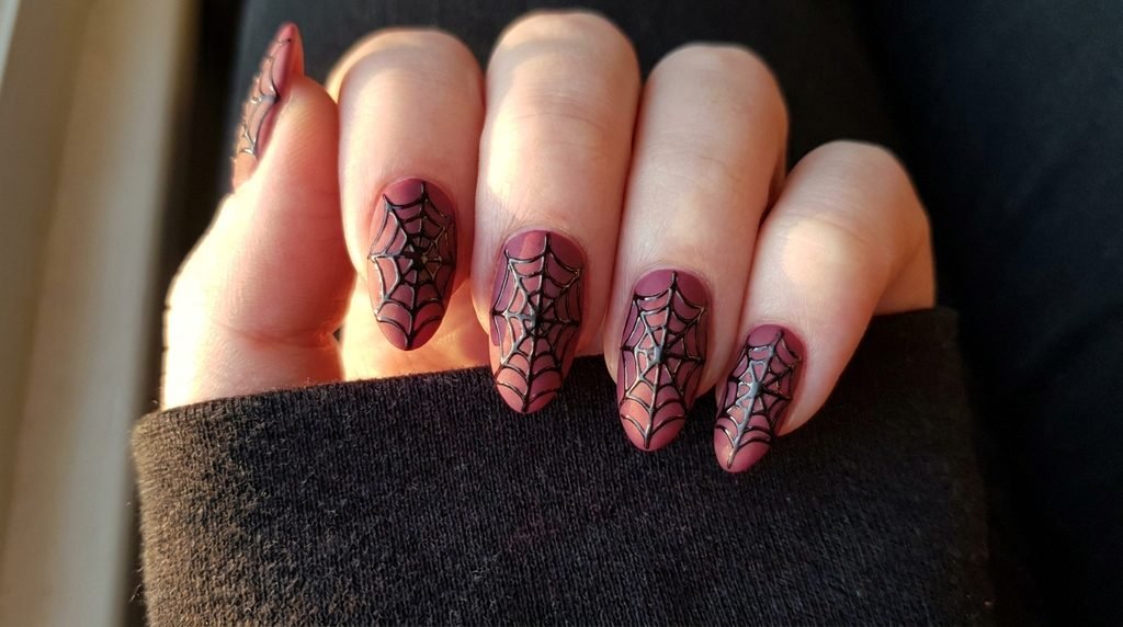 Close-up of glossy spiderweb line art painted over a velvet matte black nail on an 18-year-old female with very white skin.