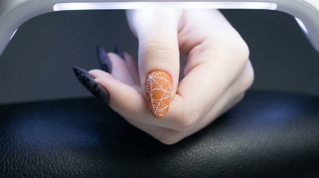 Extreme close-up of an 18-year-old female hand with white skin featuring an index nail with fine black spiderweb line art.