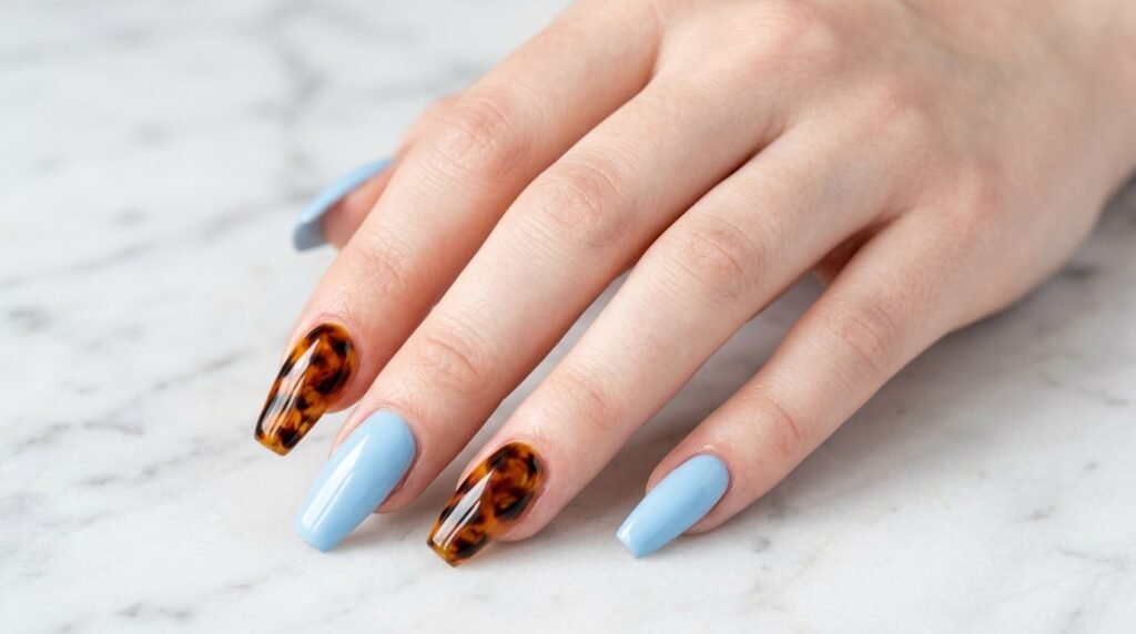 Extended female hand with very white skin showing dusty blue almond nails and one dark brown accent nail.