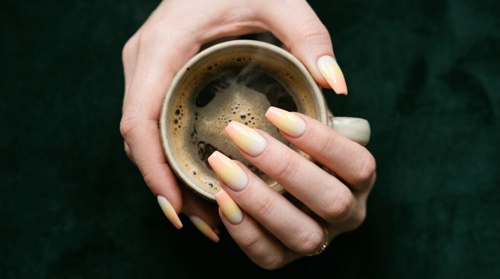 Tapered coffin nails featuring a soft white, yellow, and peach gradient on a female hand with very white skin.