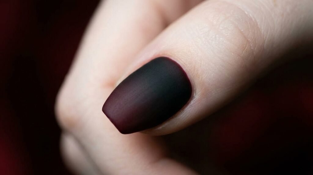 Extreme macro close-up of a seamless matte black to burgundy ombré gradient on a coffin thumbnail, on a white female hand