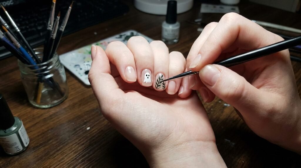 Female hand holding a fine detail brush painting botanical lines on squoval nails.