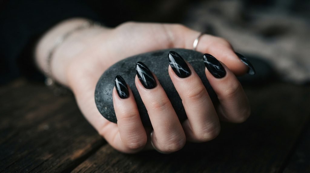 Almond-shaped smoky black marble nails cupping a dark stone on an 18-year-old female hand with white skin.