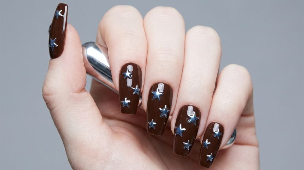 Long coffin chocolate brown nails with tiny reflective chrome blue star art on a young female hand with very white skin tone.