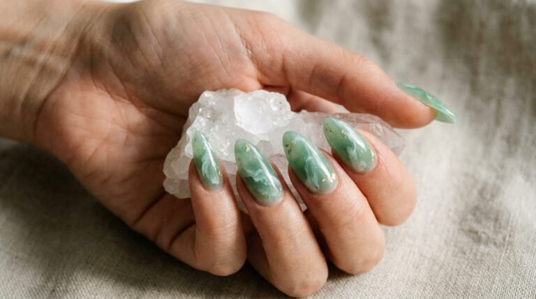 Close-up of a hand with almond-shaped jade marble nails holding a clear quartz crystal.
