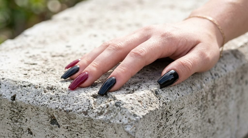 Close-up of long black and wine-red coffin nails on an 18-year-old white female hand resting on gray concrete.