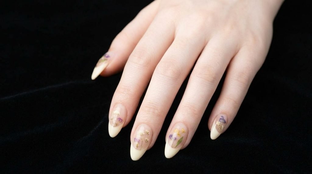 Long almond-shaped mismatched French tip nails with flowers on a female hand with white skin over matte black