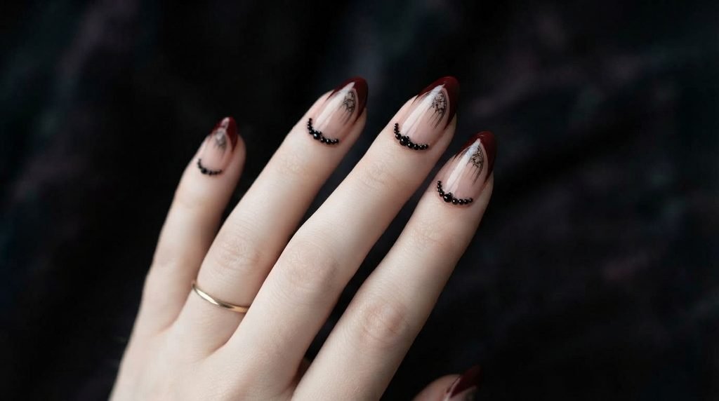 A close-up photograph showing an almond nail with an oxblood pointed French tip and a subtle black line drawing of a gothic arch detail