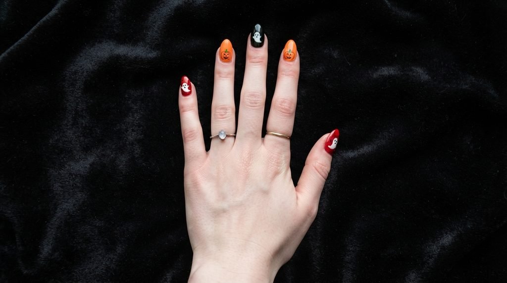 Overhead view of an 18-year-old female hand with very white skin showing balanced red, orange, and black Halloween nails.