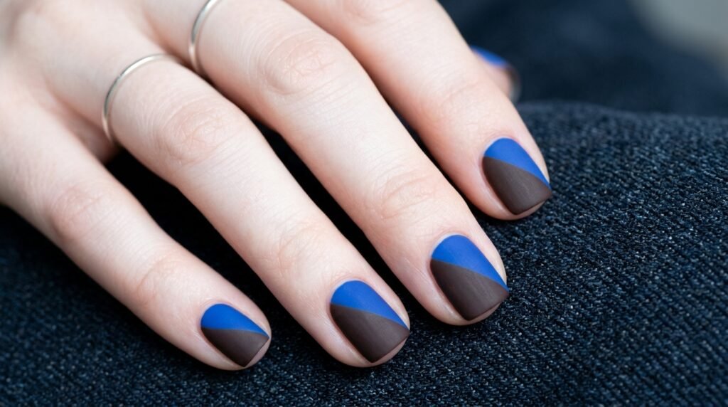 Short square nails with matte brown and bright blue color blocking on a young female hand with white skin.