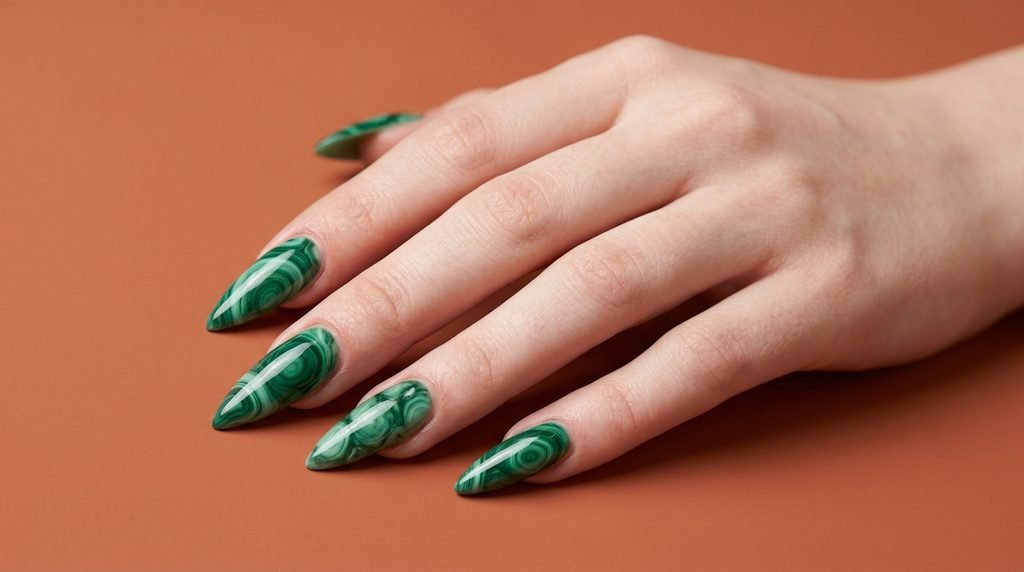Eighteen year old female hand showing translucent emerald malachite marble stiletto nails resting on a matte terracotta background.