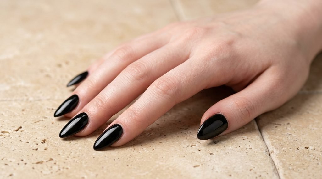 High-gloss opaque black gel nails on white skin female hand resting flat on dark cream tile background.