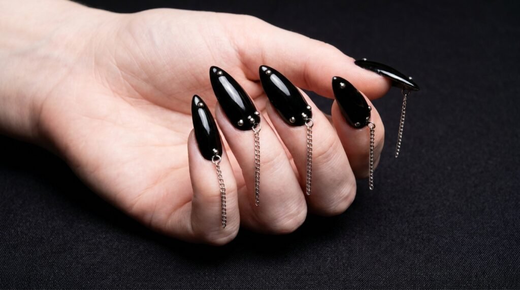 Black stiletto acrylic nails featuring hanging tip chain piercing on 18 year old hand with white skin.