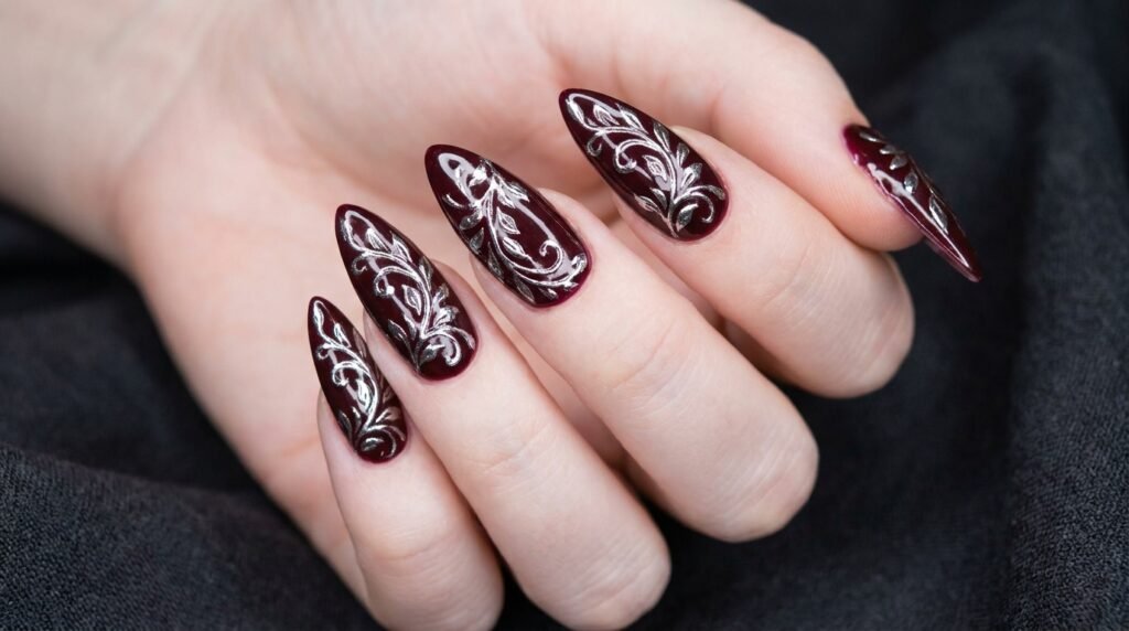 Silver chrome abstract flower linework painted on burgundy stiletto nails on very white skin.