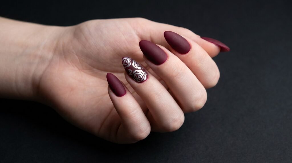 Matte burgundy stiletto nails with hand-painted silver rose art on very white skin.