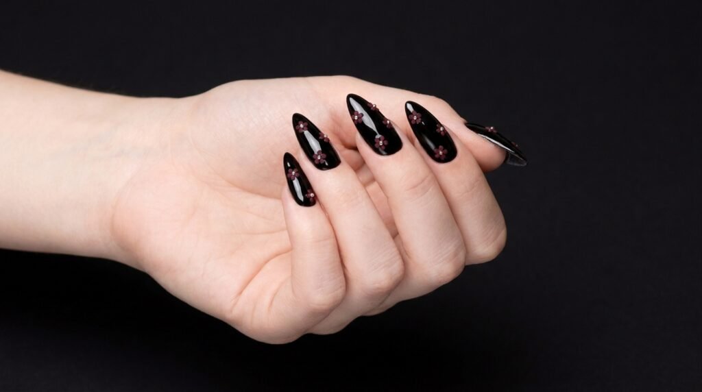 Glossy black stiletto nails featuring tiny burgundy flowers on very white skin.