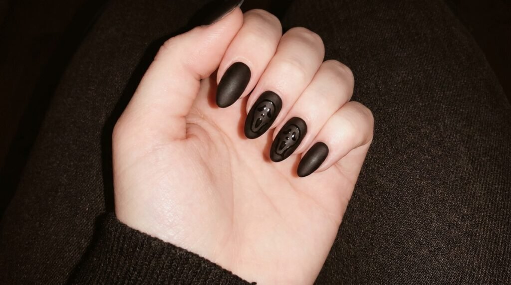 Matte black almond nails with glossy ghost mask detailing on light white skin.