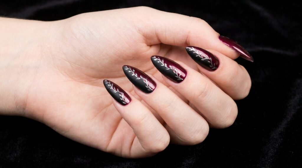 Split color burgundy and black stiletto nails with silver floral center line on very white skin.